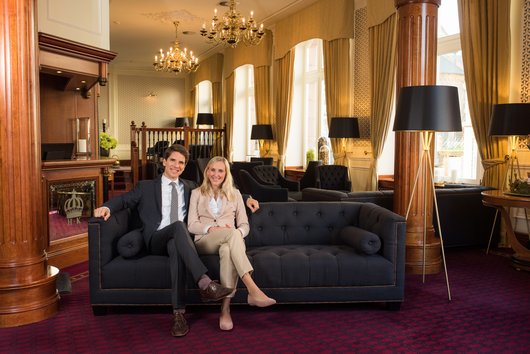 Herr und Frau Miller sitzen auf einer Couch im Foyer des Hotels